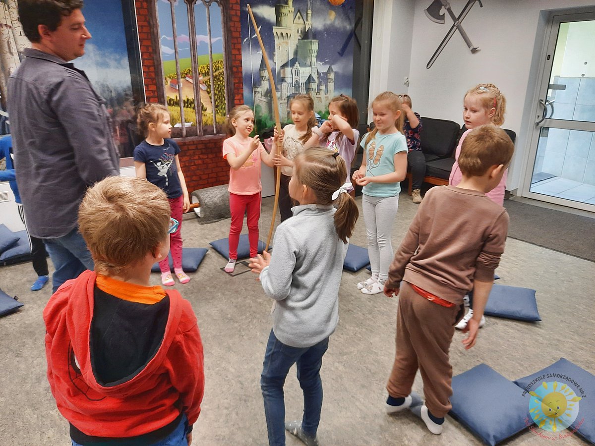 Kilkoro dzieci stoi bok dziewczynki trzymającej łuk - Przedszkole Samorządowe Nr 2 Pod Słonkiem w Białymstoku