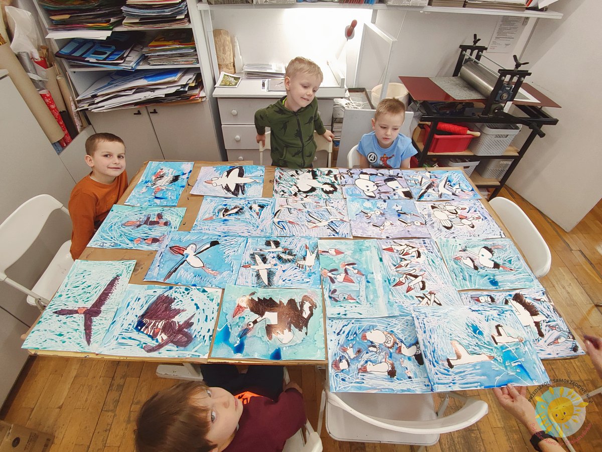 Na stole leżą namalowane prace dzieci przedstawiające bociany - Przedszkole Samorządowe Nr 2 Pod Słonkiem