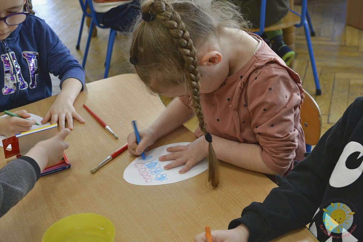 Dziewczynki siedzą przy stole i kolorują kartkę w kształcie jajka - Przedszkole Samorządowe Nr 2 Pod Słonkiem w Białymstoku