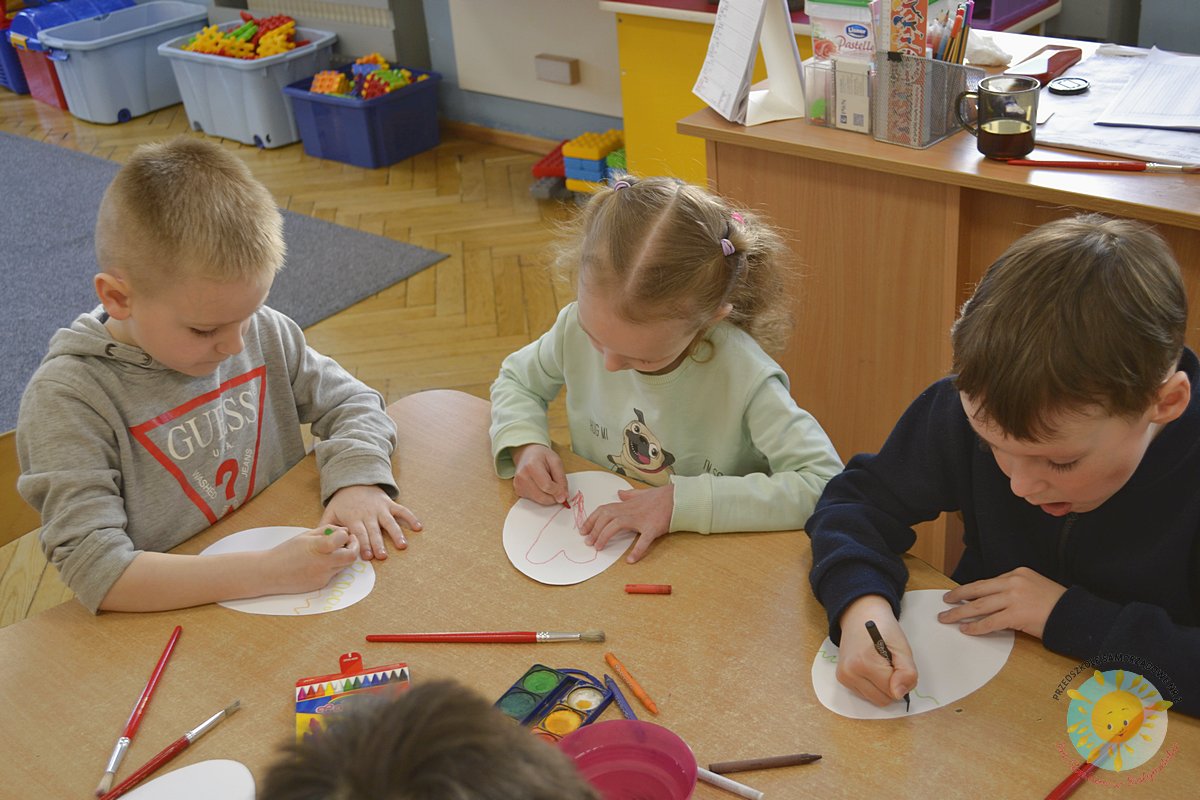 Grupa dzieci siedzi przy stole i koloruje kartkę w kształcie jajka - Przedszkole Samorządowe Nr 2 Pod Słonkiem w Białymstoku