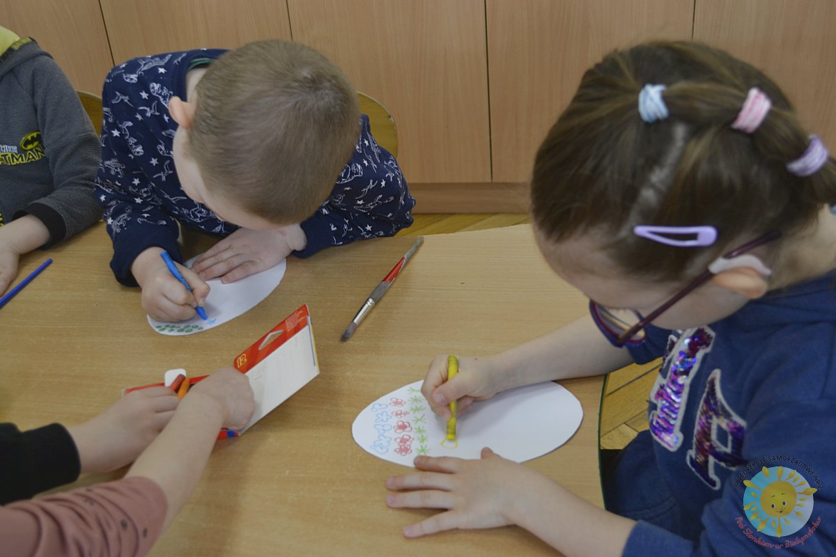 Grupa dzieci siedzi przy stole i koloruje kartkę w kształcie jajka - Przedszkole Samorządowe Nr 2 Pod Słonkiem w Białymstoku