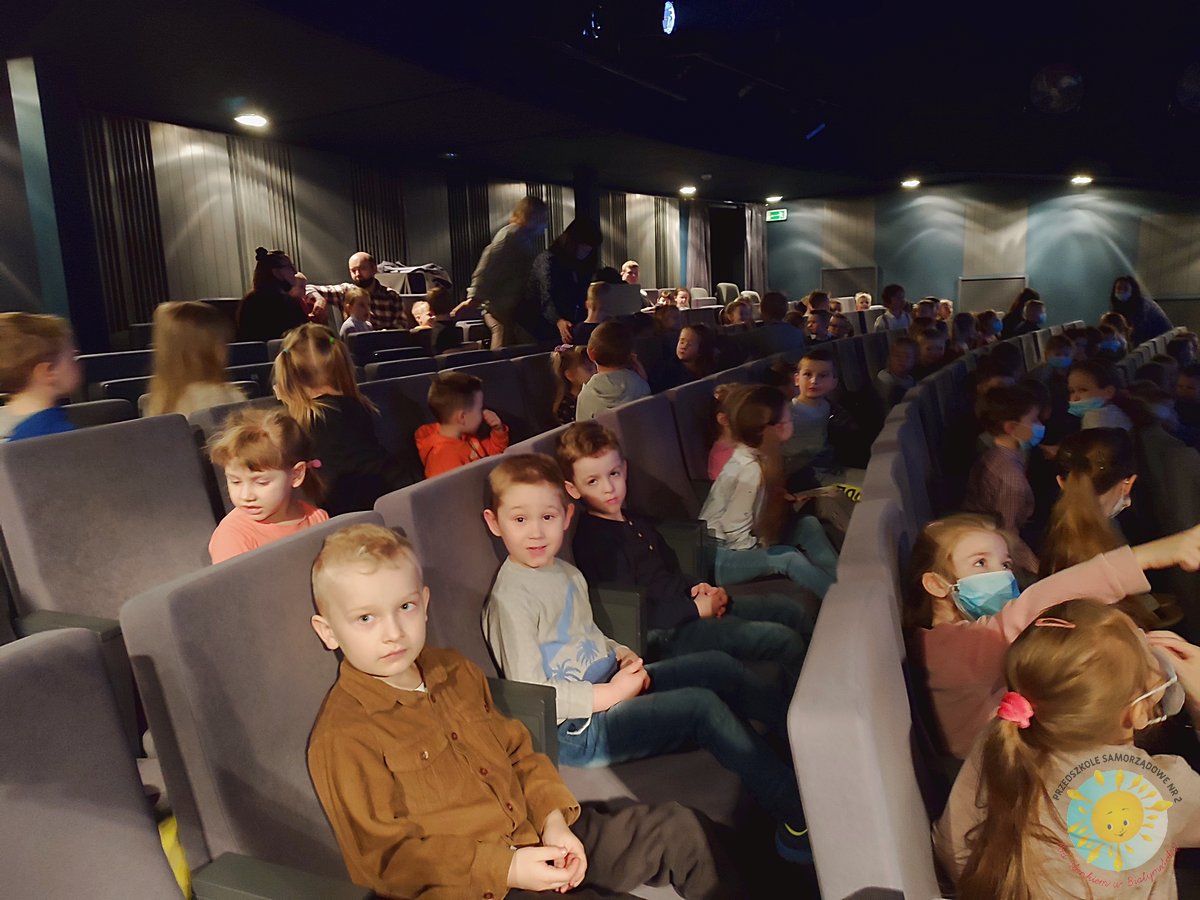 Dzieci siedzą w teatrze, wpatrując się w obiektyw aparatu - Przedszkole Samorządowe Nr 2 Pod Słonkiem