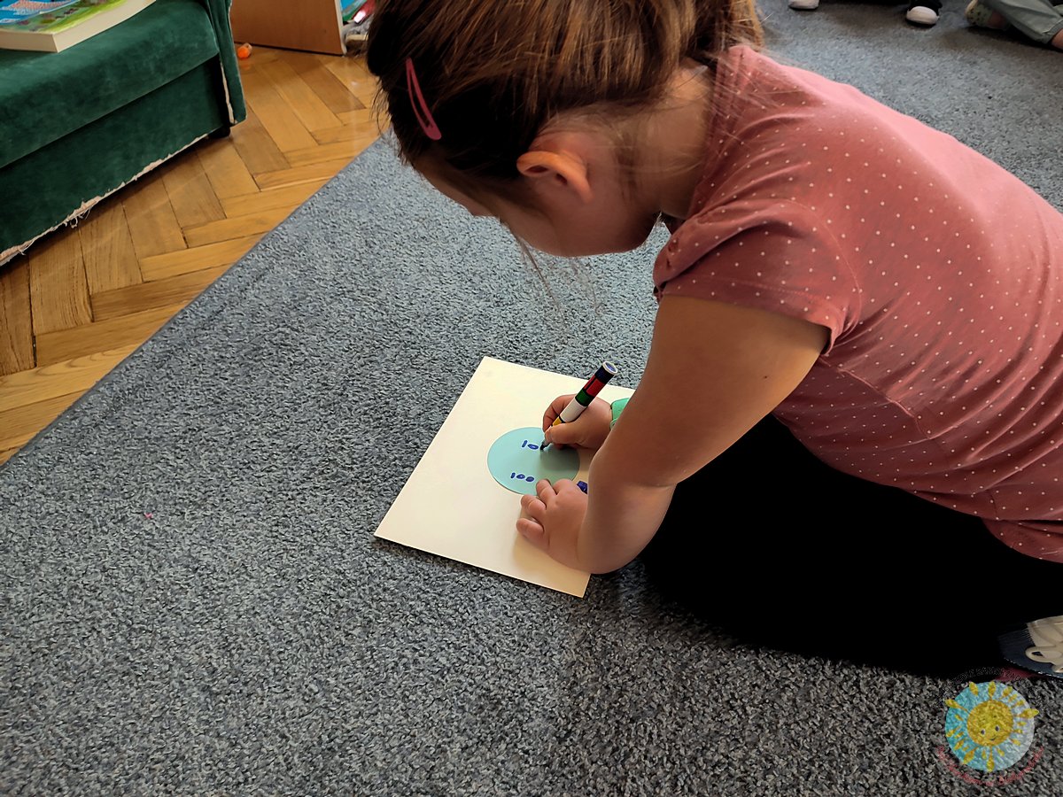 Dziecko siedzi na dywanie i zapisuje coś na kartce - Przedszkole Samorządowe Nr 2 Pod Słonkiem w Białymstoku