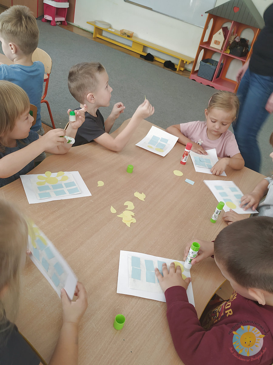 Dzieci siedzą przy stole i wyklejają na kartkach - Przedszkole Samorządowe Nr 2 Pod Słonkiem w Białymstoku