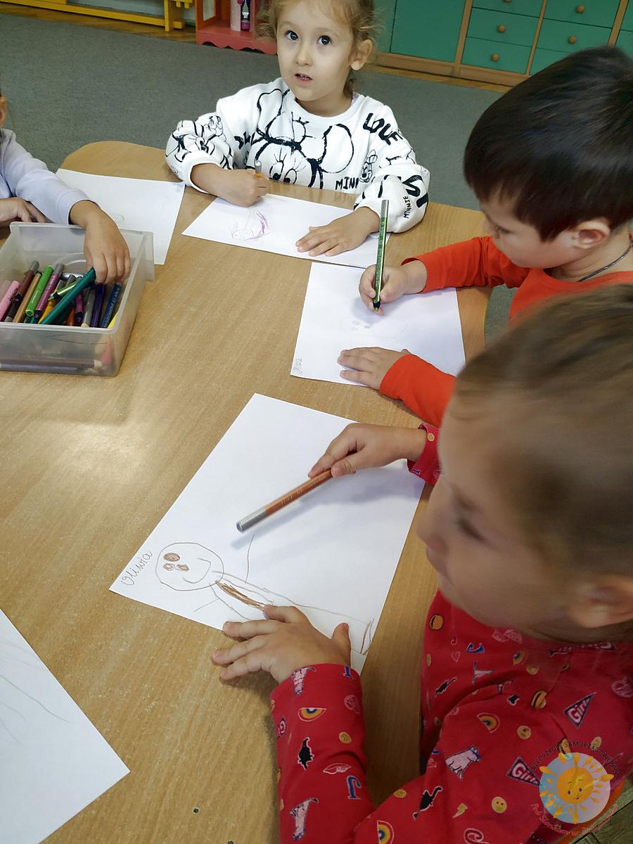 Dzieci siedzą przy stole i rysują kredkami swoją rodzinę - Przedszkole Samorządowe Nr 2 Pod Słonkiem w Białymstoku
