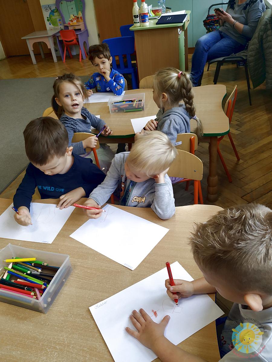 Dzieci siedzą przy stole i rysują kredkami swoją rodzinę - Przedszkole Samorządowe Nr 2 Pod Słonkiem w Białymstoku