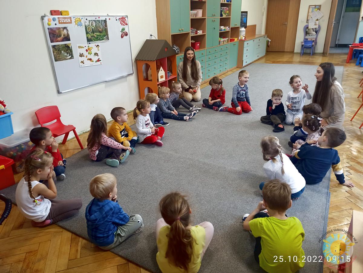 Dzieci siedzą na dywanie razem z panią, która im tłumaczy różne rzeczy - Przedszkole Samorządowe Nr 2 Pod Słonkiem w Białymstoku