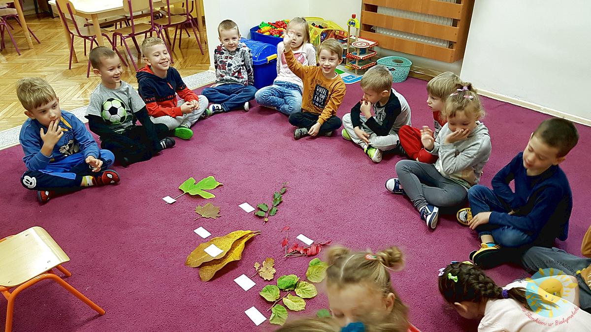 Dzieci siedzą na dywanie wkoło liści - Przedszkole Samorządowe Nr 2 Pod Słonkiem w Białymstoku