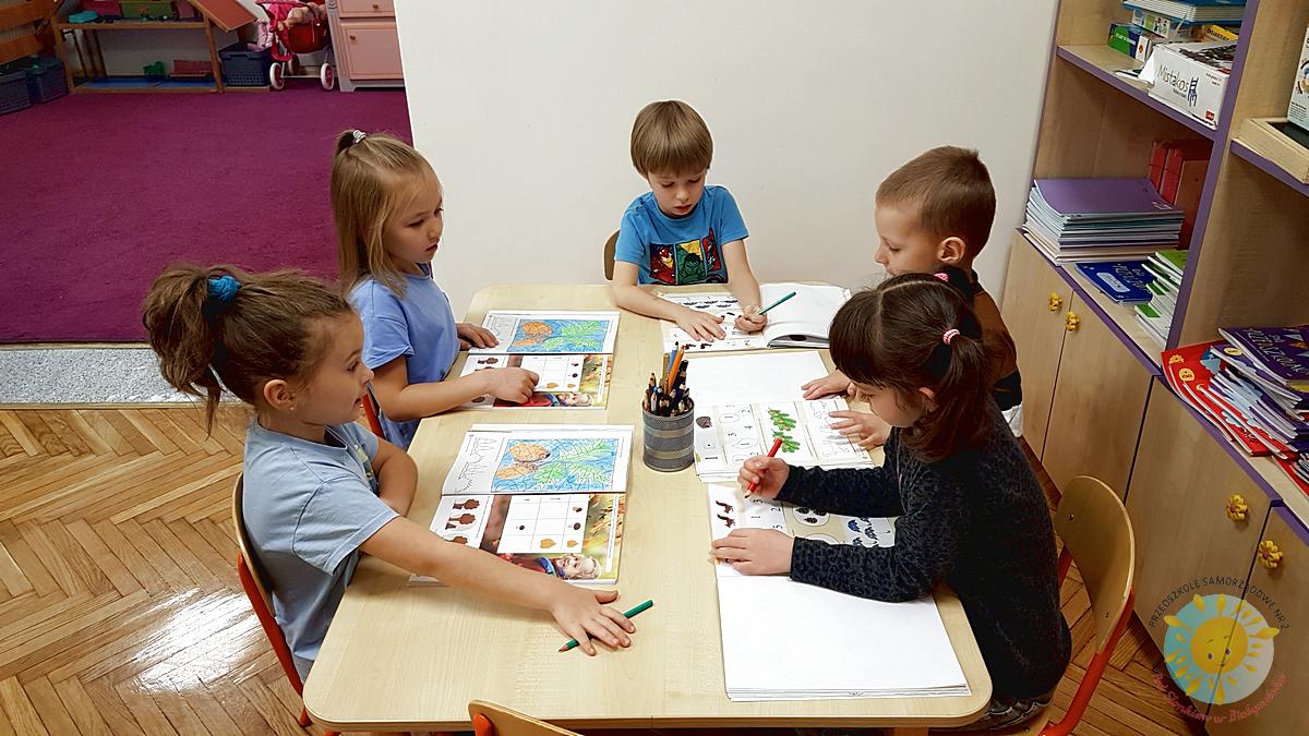 Dzieci siedzą przy stole i wykonują ćwiczenia w kartach pracy - Przedszkole Samorządowe Nr 2 Pod Słonkiem w Białymstoku