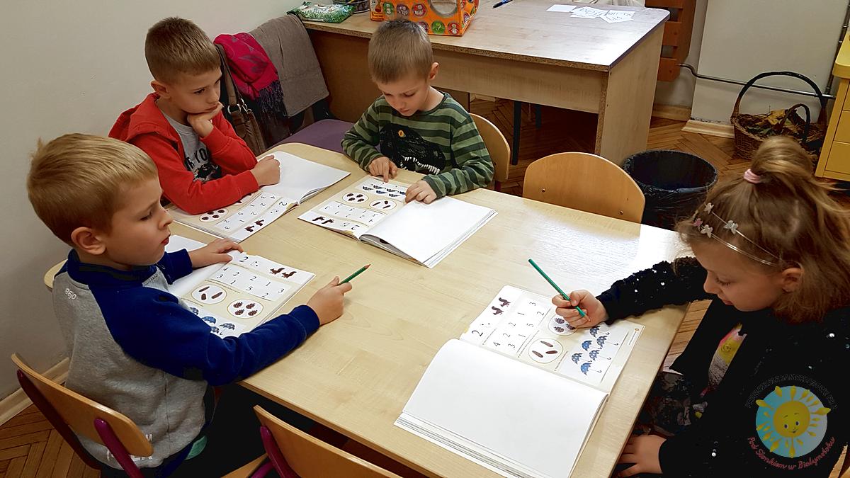 Dzieci siedzą przy stole i wykonują ćwiczenia w kartach pracy - Przedszkole Samorządowe Nr 2 Pod Słonkiem w Białymstoku