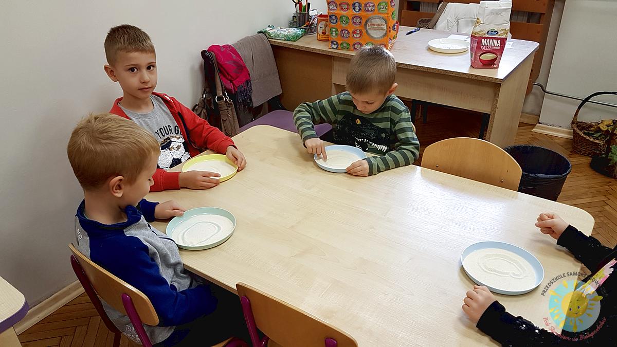 Dzieci siedzą przy stole, malują palcem w kaszy - Przedszkole Samorządowe Nr 2 Pod Słonkiem w Białymstoku
