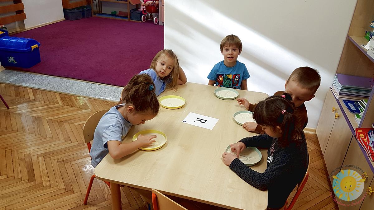 Dzieci siedzą przy stole, malują palcem w kaszy - Przedszkole Samorządowe Nr 2 Pod Słonkiem w Białymstoku