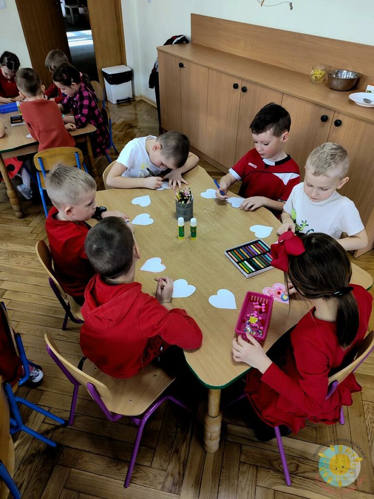 Dzieci siedzą przy stole, tworzą walentynkowe rekwizyty - Przedszkole Samorządowe Nr 2 Pod Słonkiem w Białymstoku