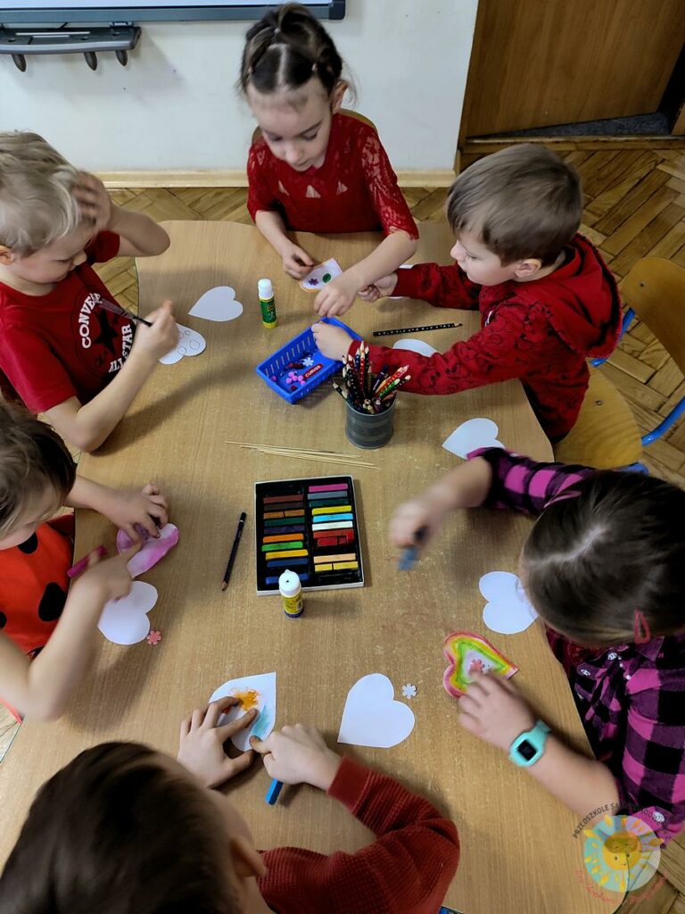 Dzieci siedzą przy stole, tworzą walentynkowe rekwizyty - Przedszkole Samorządowe Nr 2 Pod Słonkiem w Białymstoku