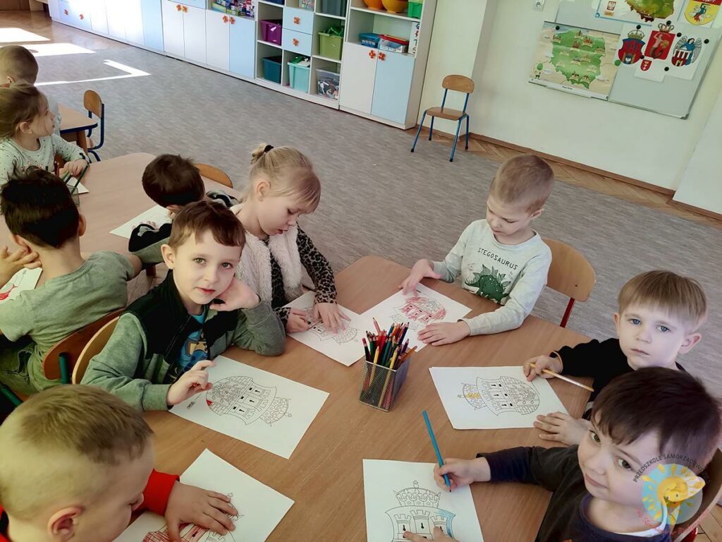 Dzieci z przedszkola siedzą przy stoliku i kolorują  herb warszawy - Przedszkole Samorządowe Nr 2 Pod Słonkiem w Białymstoku
