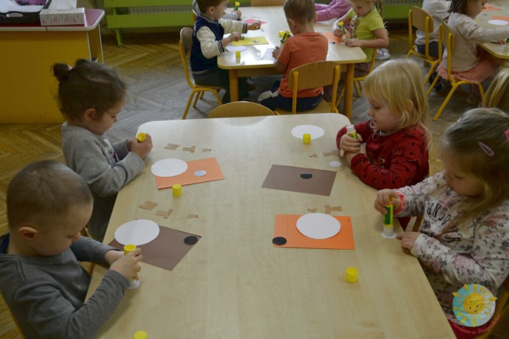 Dzieci siedzą przy stole i tworzą coś na kartkach - Przedszkole Samorządowe Nr 2 Pod Słonkiem w Białymstoku