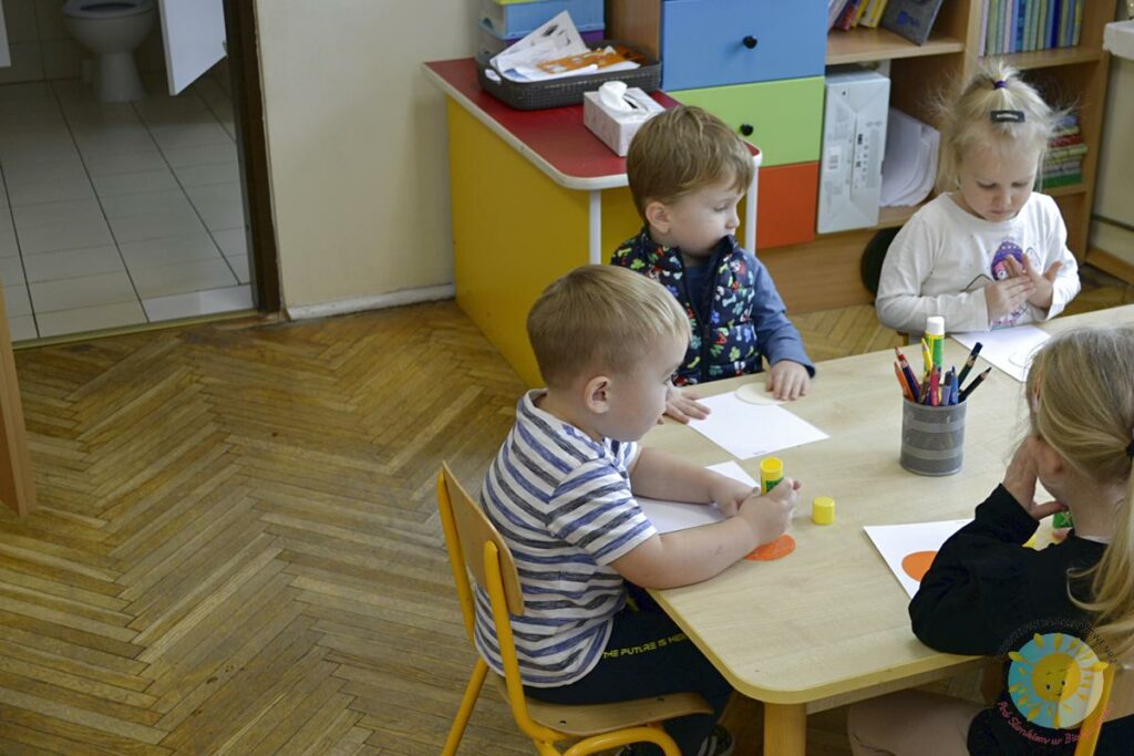 Dzieci siedzą przy stole i tworzą coś na kartkach - Przedszkole Samorządowe Nr 2 Pod Słonkiem w Białymstoku