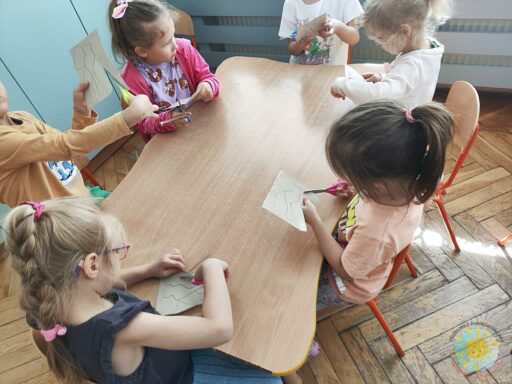 Siedzące dzieci przy stole i wykonują pracę plastyczną - Przedszkole Samorządowe Nr 2 Pod Słonkiem w Białymstoku
