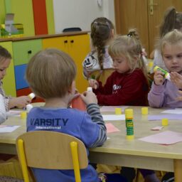 Siedzące dzieci przy stole i wykonują pracę plastyczną - Przedszkole Samorządowe Nr 2 Pod Słonkiem w Białymstoku