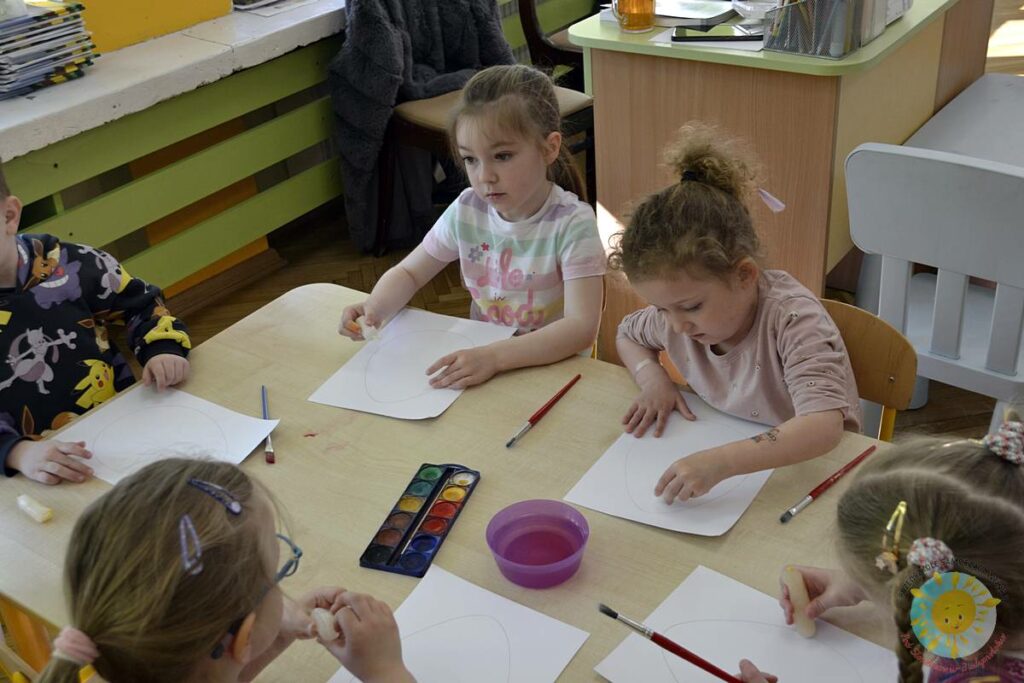 Siedzące dzieci przy przedszkolnym stoliku, wykonują pracę - Przedszkole Samorządowe Nr 2 Pod Słonkiem w Białymstoku