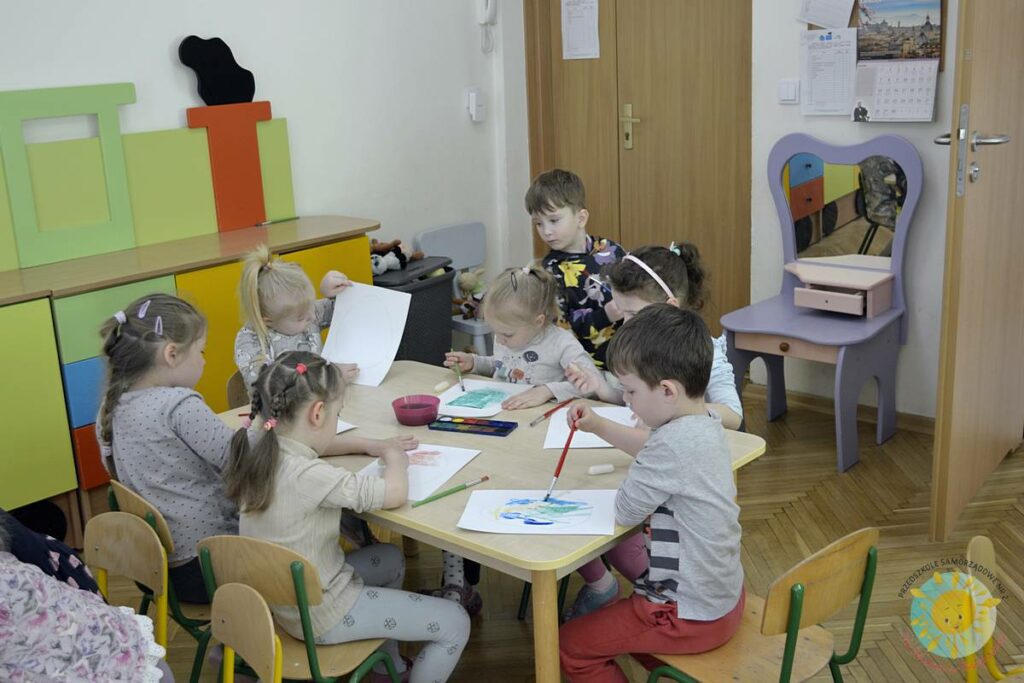 Siedzące dzieci przy przedszkolnym stoliku, wykonują pracę - Przedszkole Samorządowe Nr 2 Pod Słonkiem w Białymstoku