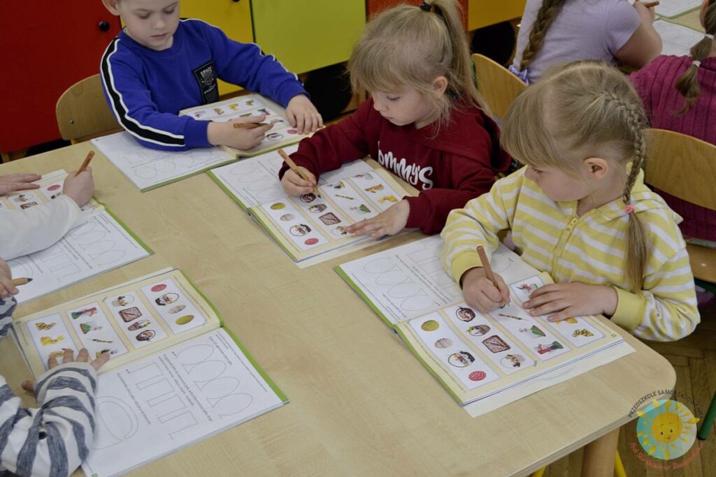 Siedzące dzieci przy przedszkolnym stoliku, wykonują pracę - Przedszkole Samorządowe Nr 2 Pod Słonkiem w Białymstoku