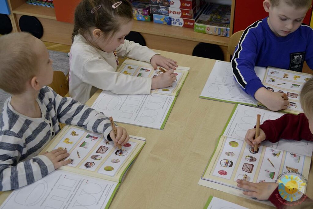 Siedzące dzieci przy przedszkolnym stoliku, wykonują pracę - Przedszkole Samorządowe Nr 2 Pod Słonkiem w Białymstoku