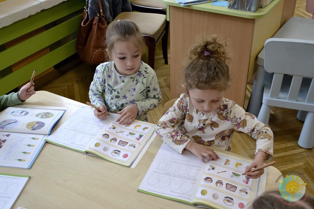 Siedzące dzieci przy przedszkolnym stoliku, wykonują pracę - Przedszkole Samorządowe Nr 2 Pod Słonkiem w Białymstoku