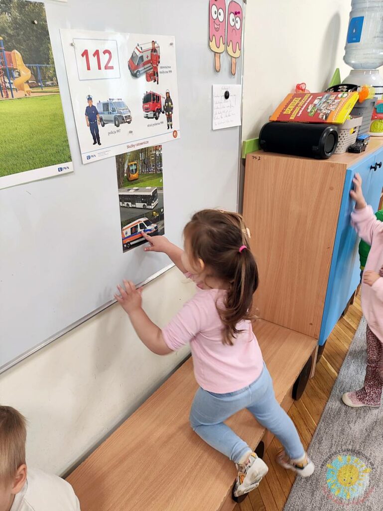 Stojące dziecko przy tablicy, wieszające obrazek - Przedszkole Samorządowe Nr 2 Pod Słonkiem w Białymstoku