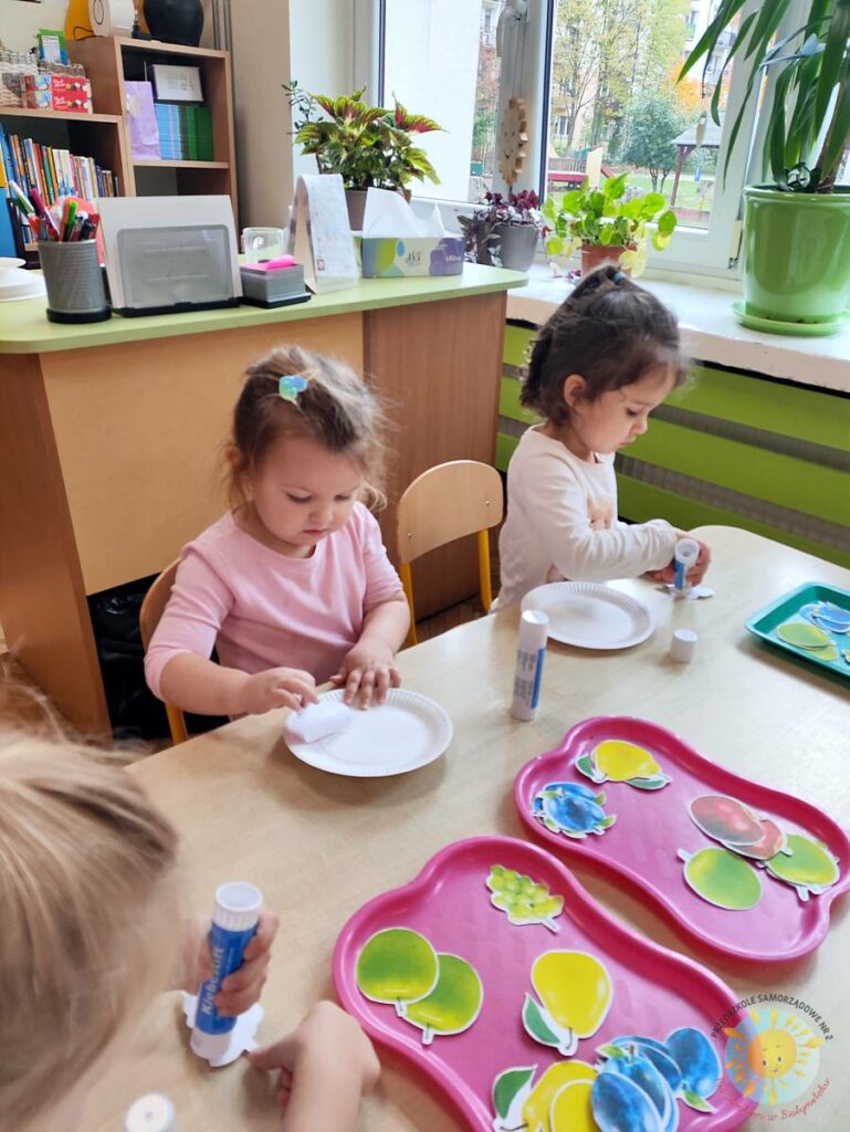 Siedzące dzieci przy stole i wykonują pracę plastyczną - Przedszkole Samorządowe Nr 2 Pod Słonkiem w Białymstoku