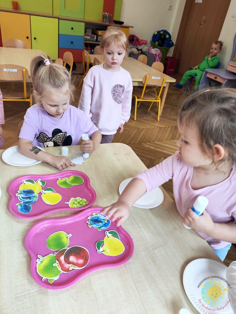 Siedzące dzieci przy stole i wykonują pracę plastyczną - Przedszkole Samorządowe Nr 2 Pod Słonkiem w Białymstoku