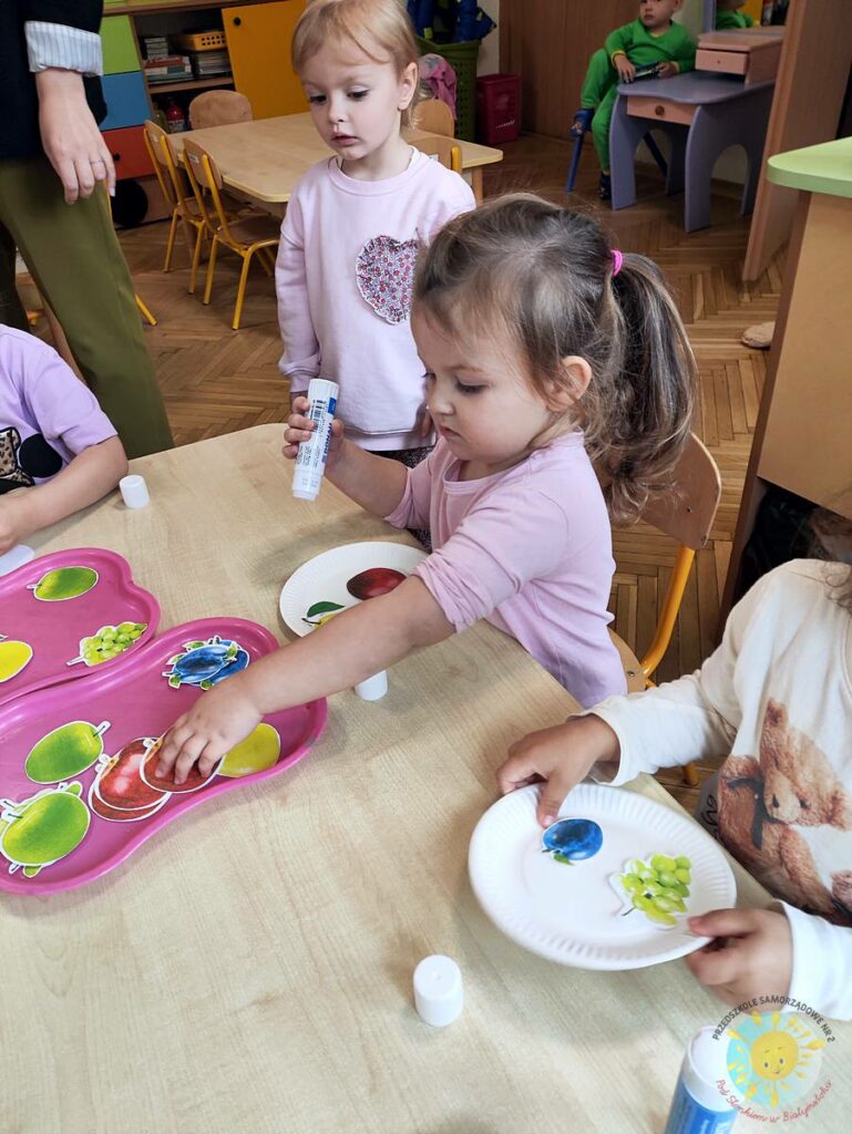 Siedzące dzieci przy stole i wykonują pracę plastyczną - Przedszkole Samorządowe Nr 2 Pod Słonkiem w Białymstoku