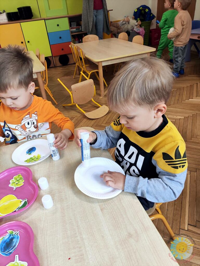 Siedzące dzieci przy stole i wykonują pracę plastyczną - Przedszkole Samorządowe Nr 2 Pod Słonkiem w Białymstoku