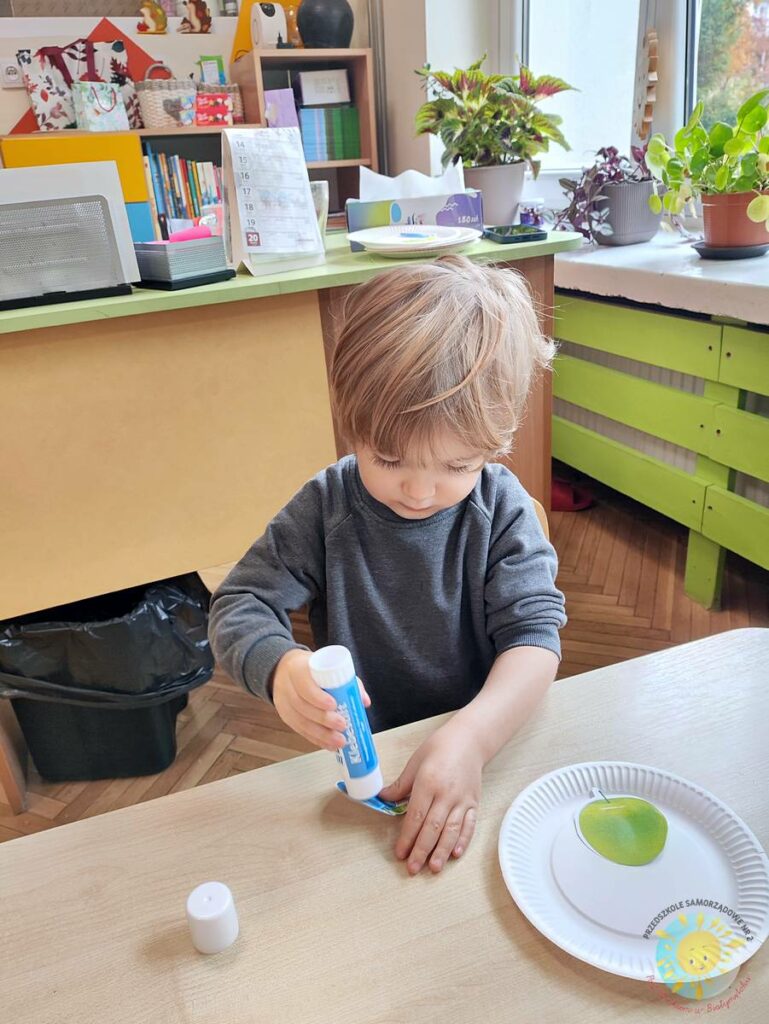 Siedzące dzieci przy stole i wykonują pracę plastyczną - Przedszkole Samorządowe Nr 2 Pod Słonkiem w Białymstoku