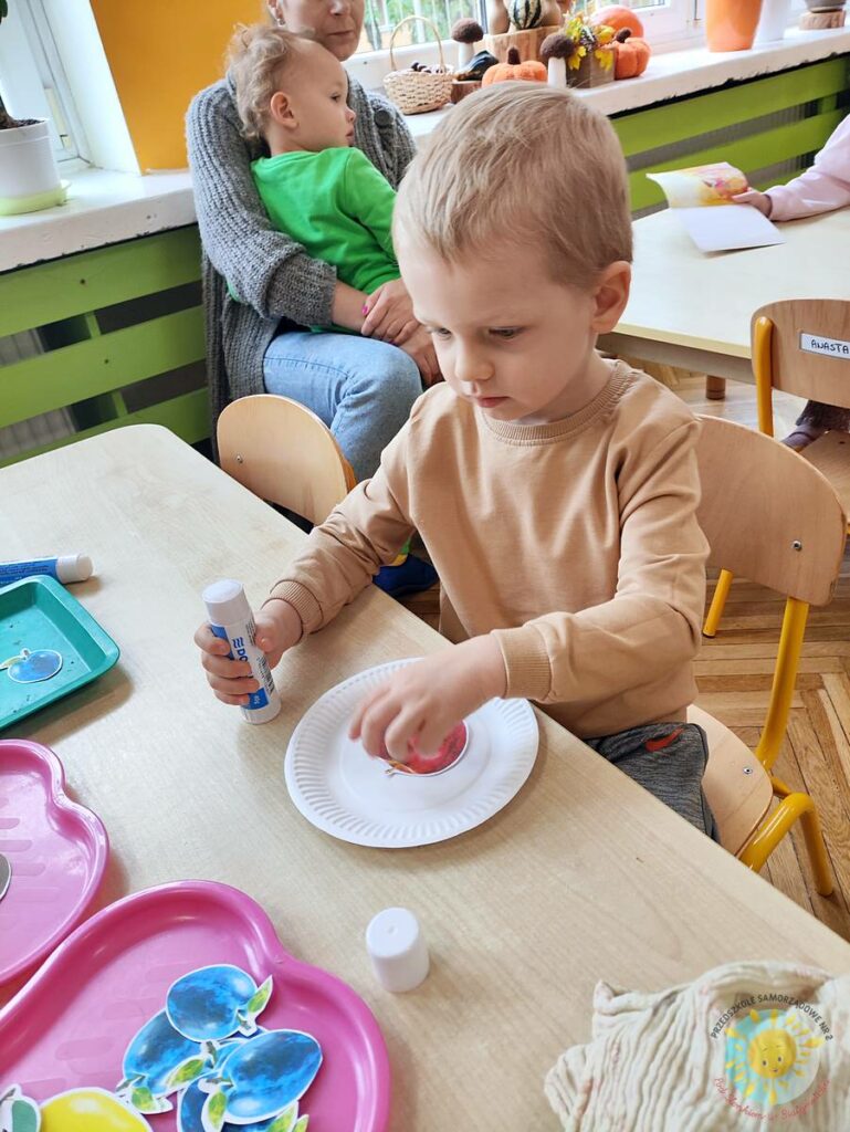 Siedzące dzieci przy stole i wykonują pracę plastyczną - Przedszkole Samorządowe Nr 2 Pod Słonkiem w Białymstoku