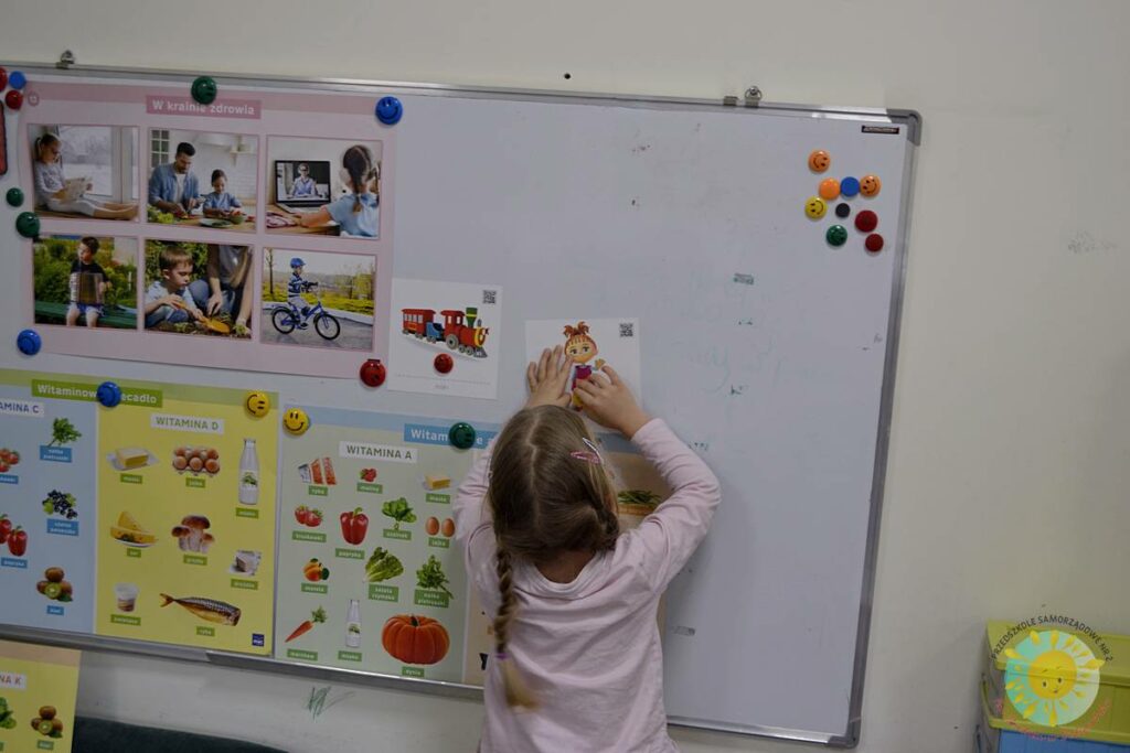Stojące dziecko przy tablicy, wieszające obrazek - Przedszkole Samorządowe Nr 2 Pod Słonkiem w Białymstoku