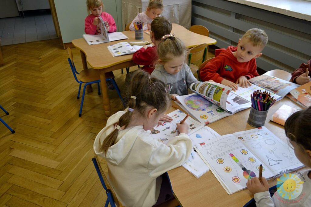 Siedzące dzieci przy przedszkolnym stoliku, wykonują pracę - Przedszkole Samorządowe Nr 2 Pod Słonkiem w Białymstoku