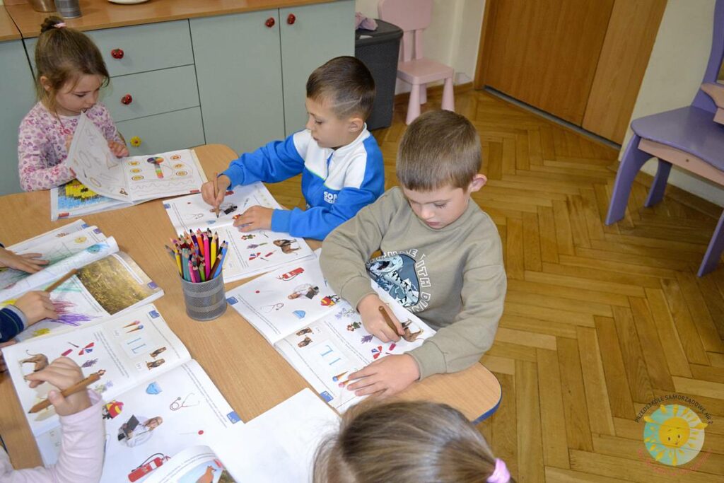 Siedzące dzieci przy przedszkolnym stoliku, wykonują pracę - Przedszkole Samorządowe Nr 2 Pod Słonkiem w Białymstoku