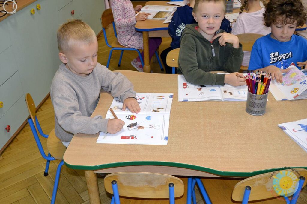 Siedzące dzieci przy przedszkolnym stoliku, wykonują pracę - Przedszkole Samorządowe Nr 2 Pod Słonkiem w Białymstoku