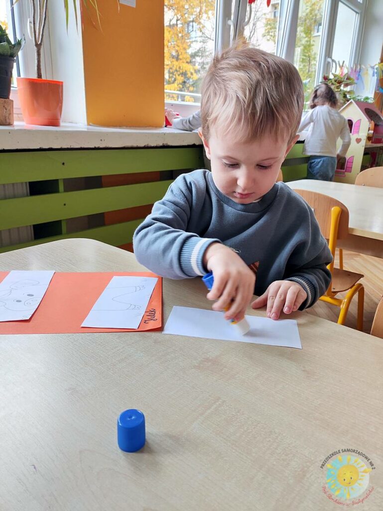 Siedzące dzieci przy przedszkolnym stoliku, wykonują pracę - Przedszkole Samorządowe Nr 2 Pod Słonkiem w Białymstoku