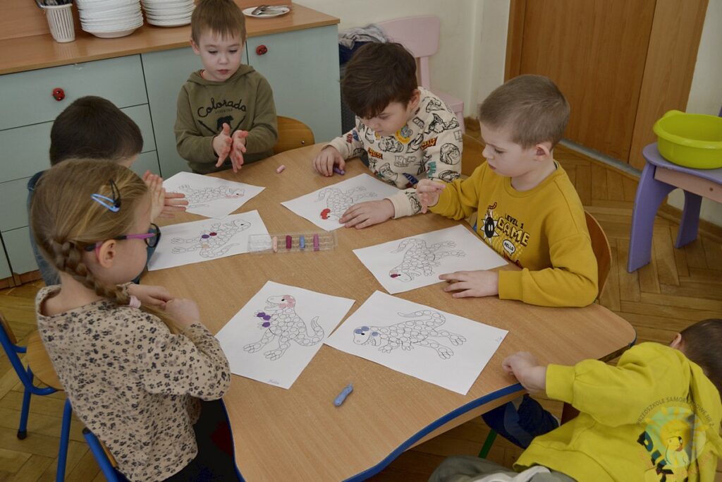 Siedzące dzieci przy przedszkolnym stoliku, wykonują pracę - Przedszkole Samorządowe Nr 2 Pod Słonkiem w Białymstoku