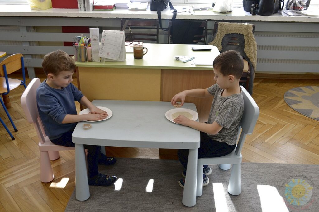 Siedzące dzieci przy przedszkolnym stoliku, wykonują pracę - Przedszkole Samorządowe Nr 2 Pod Słonkiem w Białymstoku