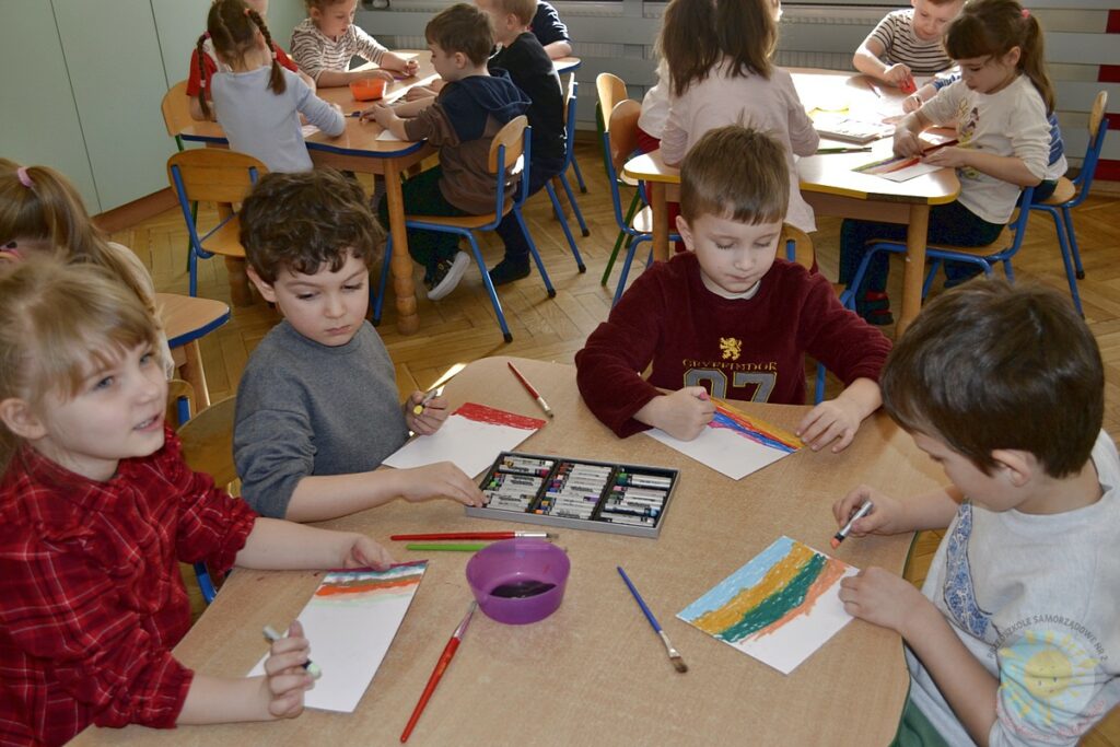Siedzące dzieci przy przedszkolnym stoliku, wykonują pracę - Przedszkole Samorządowe Nr 2 Pod Słonkiem w Białymstoku