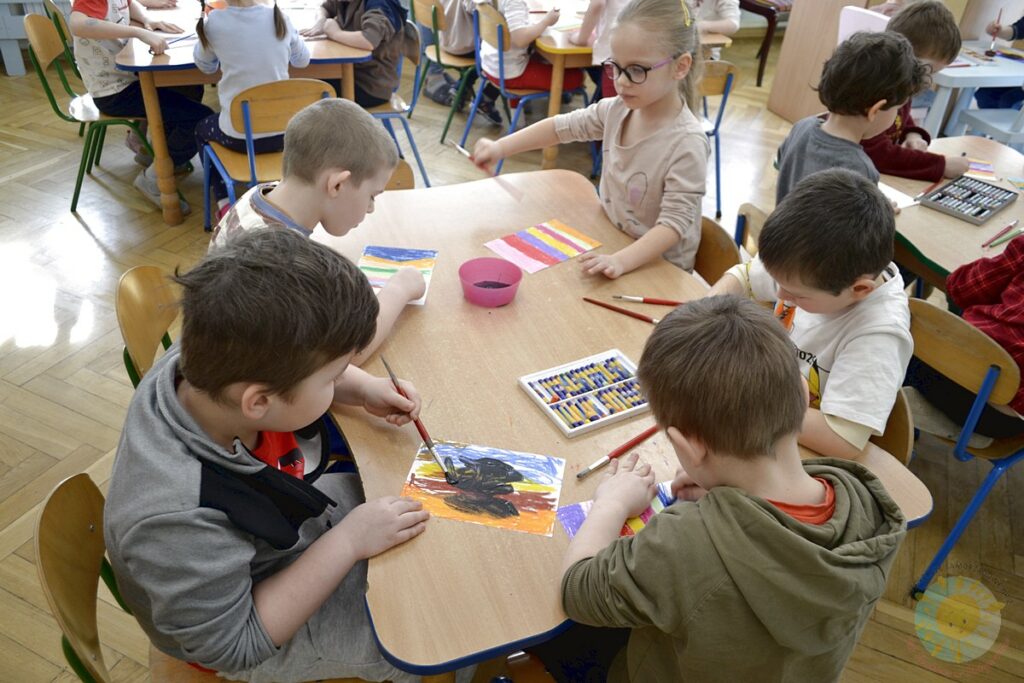 Siedzące dzieci przy przedszkolnym stoliku, wykonują pracę - Przedszkole Samorządowe Nr 2 Pod Słonkiem w Białymstoku