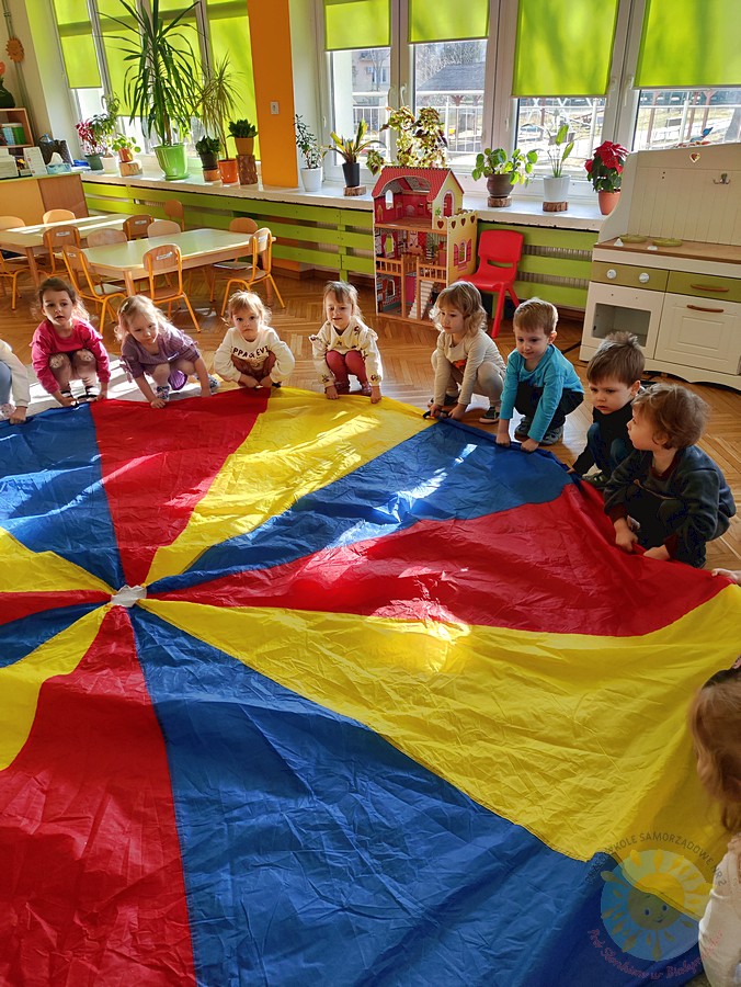 Bawiące się dzieci chustą KLANZA na dywanie przedszkolnym - Przedszkole Samorządowe Nr 2 Pod Słonkiem w Białymstoku
