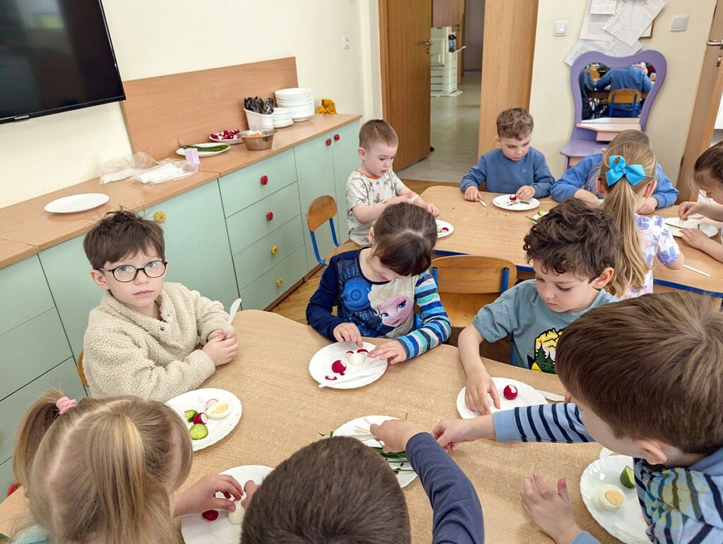 Siedzące dzieci przy stole, które biorą udział w zajęciach gastronomicznych - Przedszkole Samorządowe Nr 2 Pod Słonkiem w Białymstoku