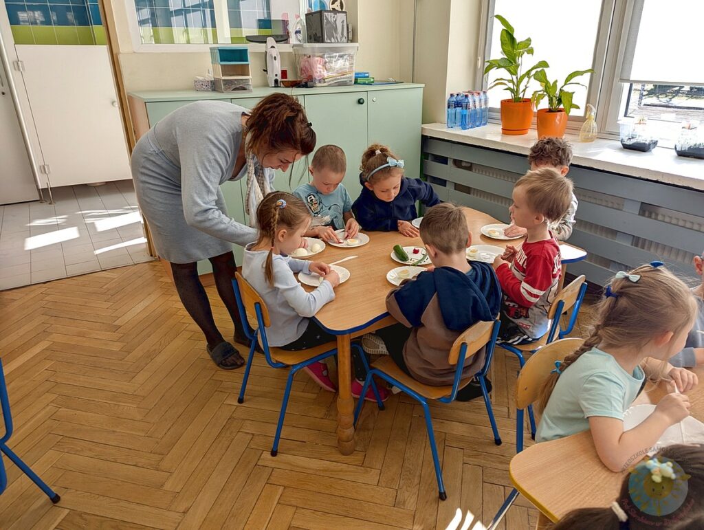 Siedzące dzieci przy stole, które biorą udział w zajęciach gastronomicznych - Przedszkole Samorządowe Nr 2 Pod Słonkiem w Białymstoku