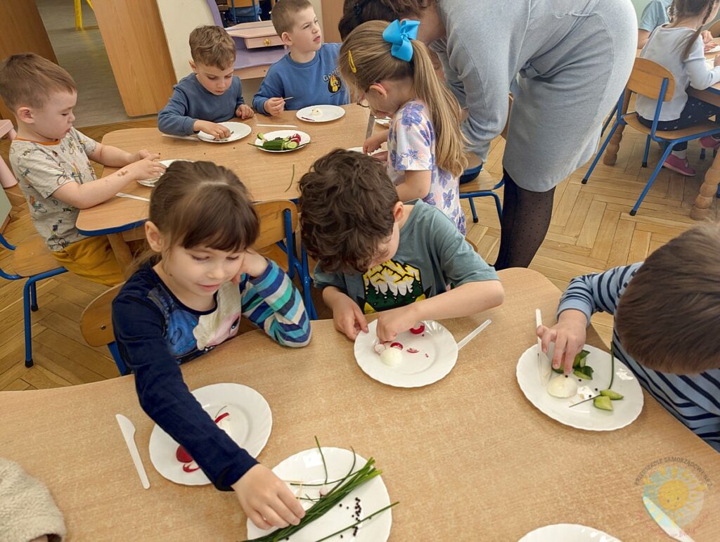 Siedzące dzieci przy stole, które biorą udział w zajęciach gastronomicznych - Przedszkole Samorządowe Nr 2 Pod Słonkiem w Białymstoku