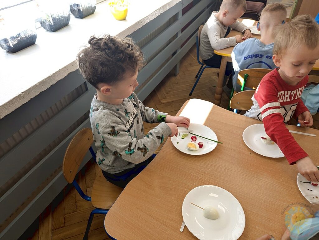Siedzące dzieci przy stole, które biorą udział w zajęciach gastronomicznych - Przedszkole Samorządowe Nr 2 Pod Słonkiem w Białymstoku