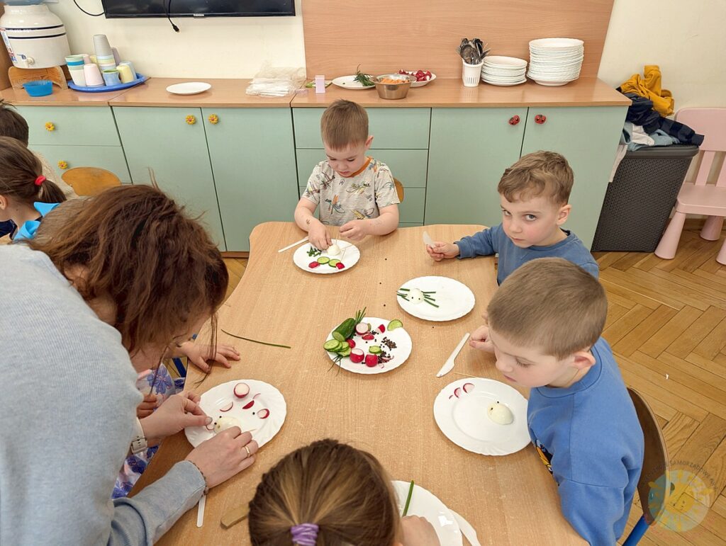 Siedzące dzieci przy stole, które biorą udział w zajęciach gastronomicznych - Przedszkole Samorządowe Nr 2 Pod Słonkiem w Białymstoku